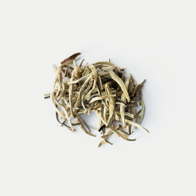 A small pile of loose leaf Jasmine Silver Needles from Rishi Tea & Botanicals rests on a white background, inviting tea connoisseurs to indulge in its delicate elegance.