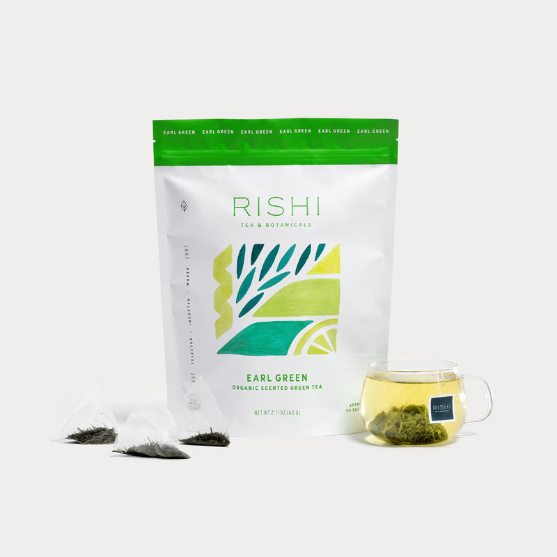 A package of Rishi Tea & Botanicals Earl Grey green tea with two tea bags and a glass cup of brewed Japanese sencha green tea in front.