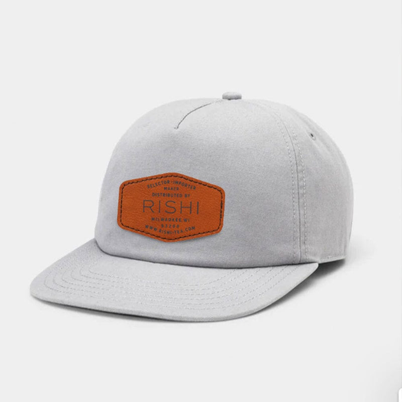 Introducing the Rishi Logo Hat by Rishi Tea & Botanicals, a light gray baseball cap made from 100% organic cotton, featuring a brown patch with text on the front and offering adjustable sizing.