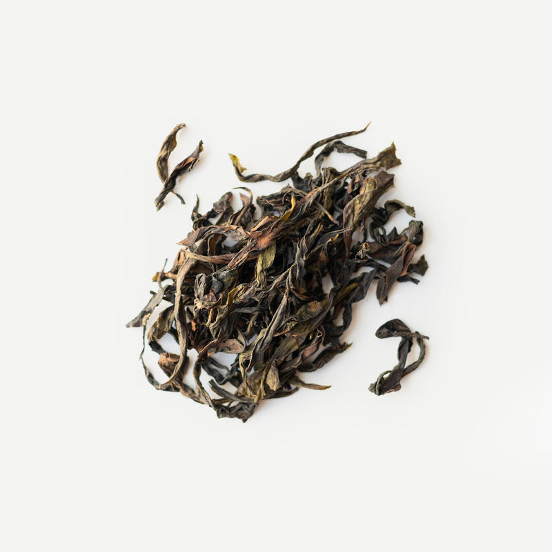 Loose dried Wuyi oolong tea leaves from Rishi Tea & Botanicals are arranged on a white background, suggesting their floral aroma and nectar-like sweetness.