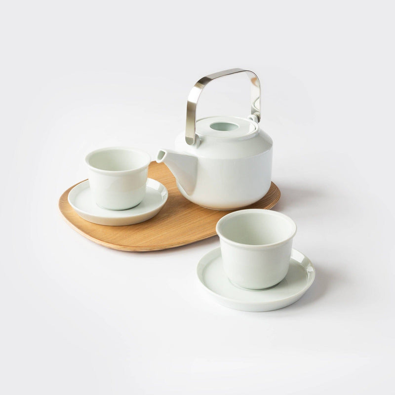 The Rishi Tea & Botanicals Hasami Porcelain Tea Set includes a handcrafted white teapot with a metal handle, paired with two elegant white cups and saucers on a non-slip wood serving tray against a plain background.