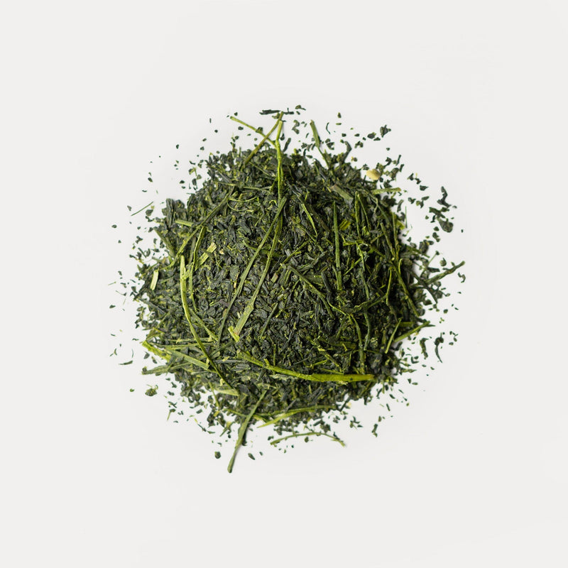 Loose organic shincha green tea leaves from Rishi Tea & Botanicals are arranged in a small, circular pile on a white background, emphasizing their full-bodied flavor and aromatic notes.